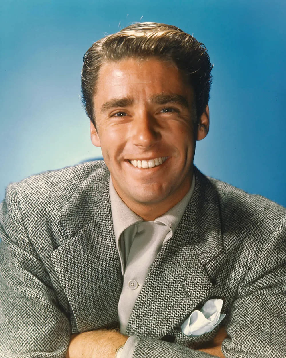 A close-up photo of Peter Lawford smiling in a grey suit