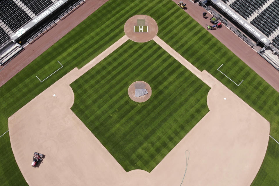 In an otherwise empty ballpark, grounds crew members continue to keep the Seattle Mariners' field in playing shape as baseball goes into its seventh week without play because of the coronavirus outbreak, Monday, May 11, 2020, in Seattle. A person familiar with the decision tells The Associated Press that Major League Baseball owners have given the go-ahead to making a proposal to the players' union that could lead to the coronavirus-delayed season starting around the Fourth of July weekend in ballparks without fans. (AP Photo/Elaine Thompson)