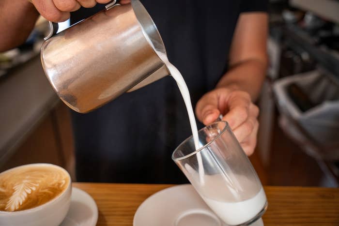 A barista pouring milk into a glass