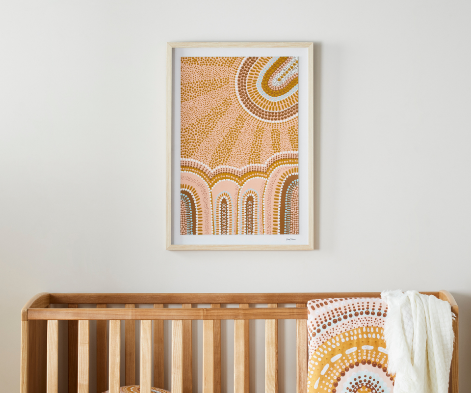 An indigenous dotted painting is framed on a white wall above a timber cot with a matching patterned blanket over the top of the cot.https://fave.co/3iwZUzc