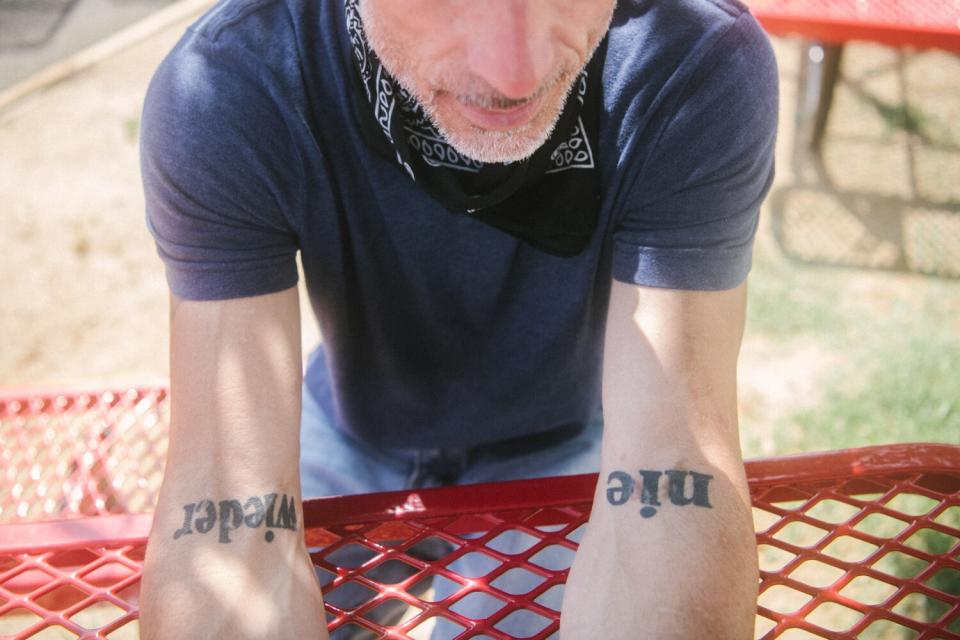 A man shows the tattoos on his arms.