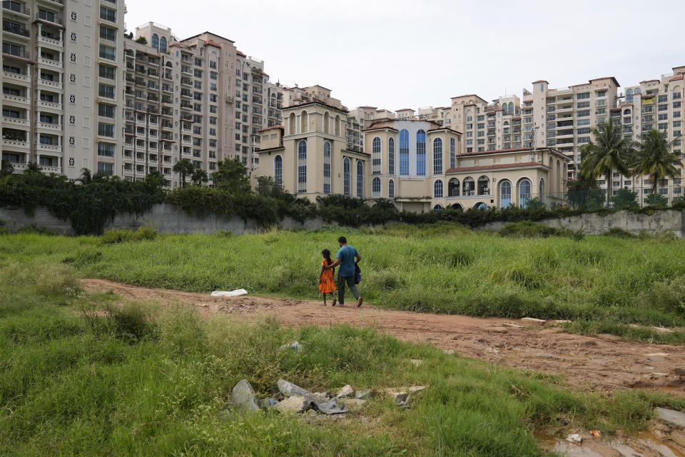 Jaidul Islam, right, walks past an upscale residential apartment building with his daughter Jerifa to drop her at a government school in Bengaluru, India, Wednesday, July 20, 2022. A flood in 2019 in the Darrang district of India's Assam started Jerifa Islam, her brother Raju and their parents on a journey that led the family from their Himalayan village to the poor neighborhood.(AP Photo/Aijaz Rahi)