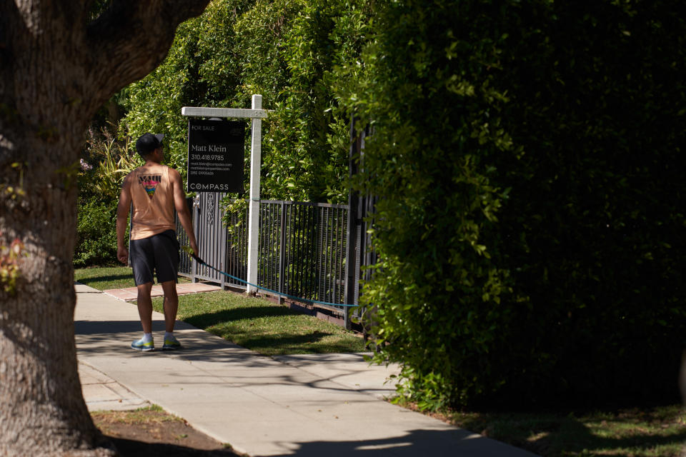 Un hombre pasea con su perro delante de un cartel. 