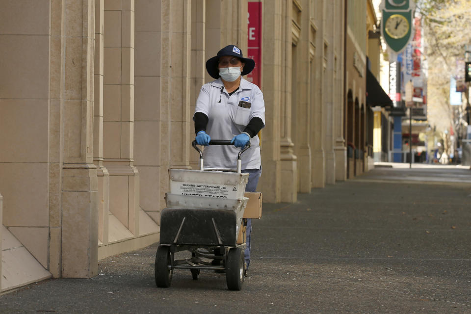 FILE - In this Wednesday, March 25, 2020 file photo, U.S Postal carrier Jasmine Yang wears a mask and gloves as preventative measures against the coronavirus, as she delivers the mail in Sacramento, Calif. Health experts say the risks are very low that coronavirus will remain on envelopes or packages and infect anyone that comes in contact with it. But those on the frontlines of all those deliveries are taking steps to try to protect themselves. (AP Photo/Rich Pedroncelli)