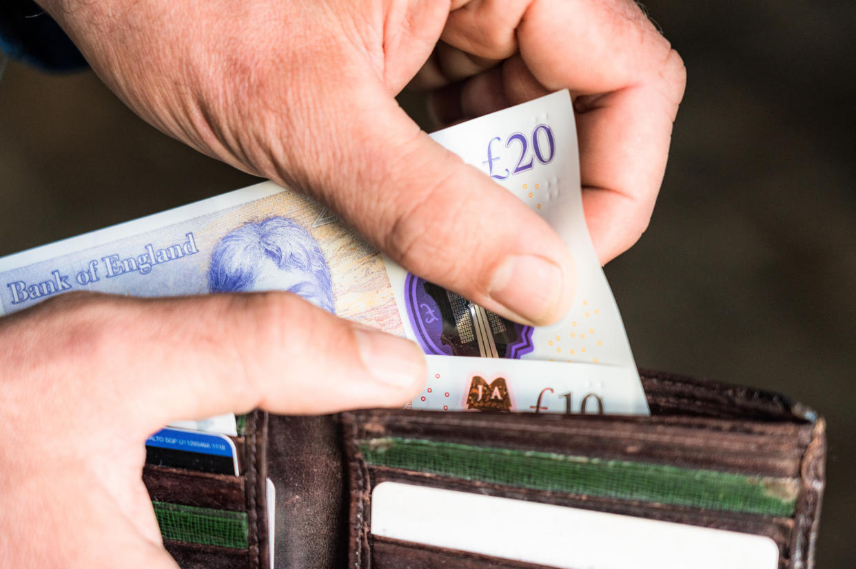 Close-up of a man taking a British twenty pound note out of his wallet.