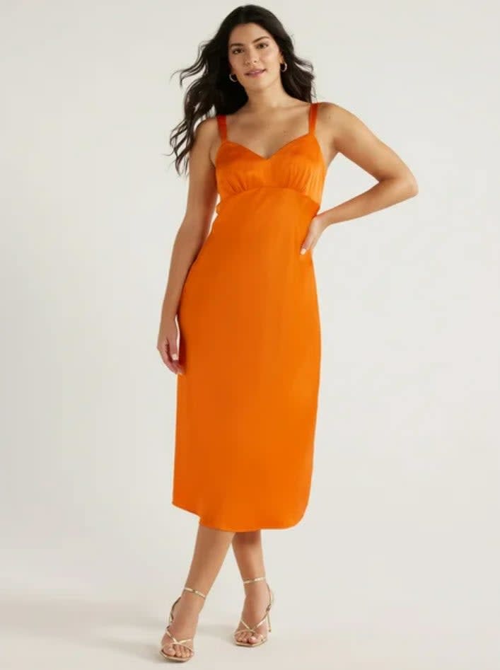 model in a sleeveless orange midi dress and strappy heels, posing with hand on hip