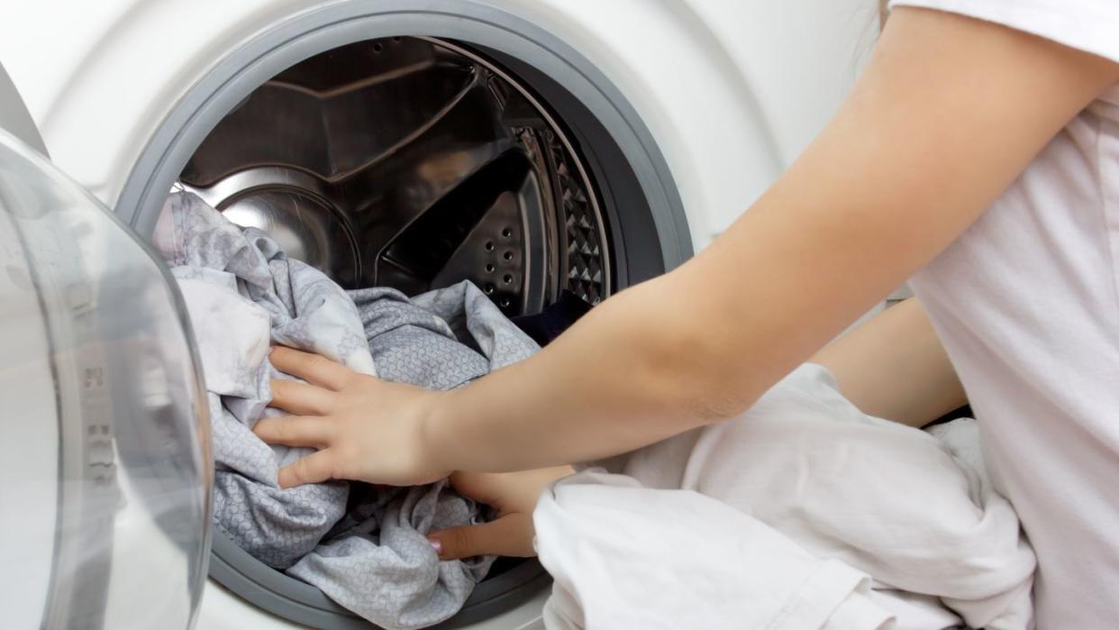 hands of a young girl put clothes in the washing machine drum