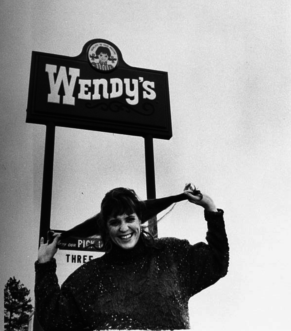 woman pulling her hair in two pigtails standing in front of the wendy's sign