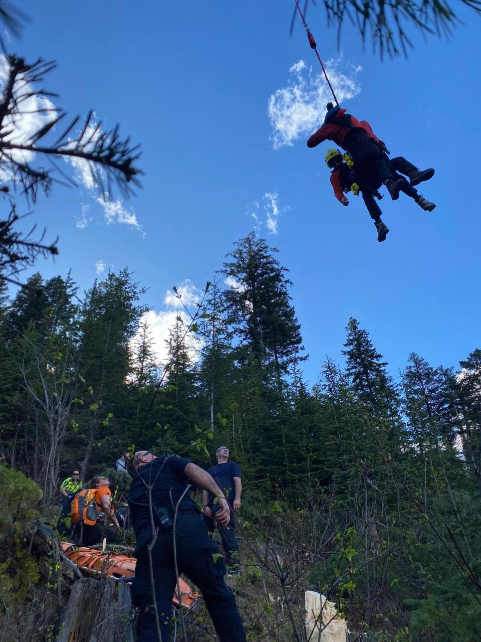 Search and rescue crew members look up as rescue personnel descend from a rescue helicopter Thursday during an operation to extract a man attacked by a grizzly bear from steep, complex terrain near the B.C.-Alberta border. (Submitted by Elkford Search and Rescue - image credit)