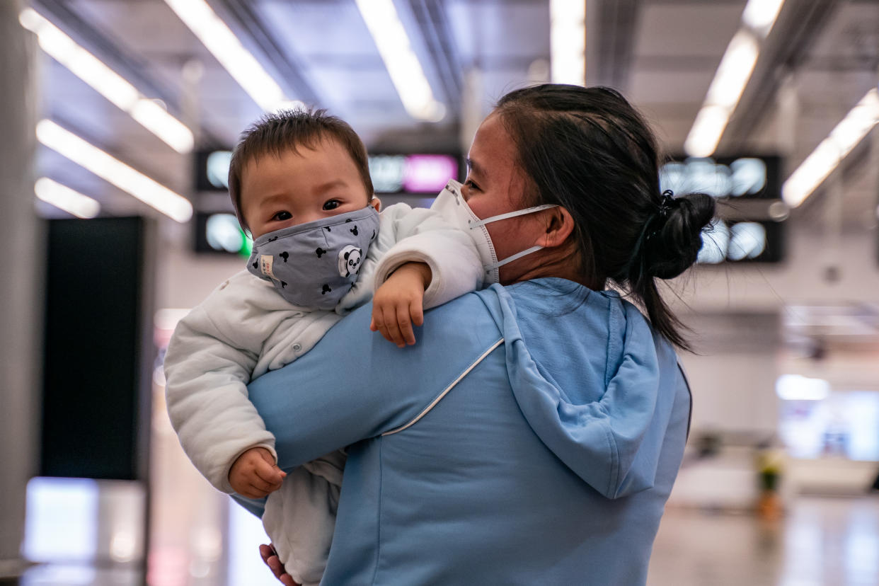 HONG KONG, CHINA - JANUARY 29: A woman carries a baby wearing a protective mask as they exit the arrival hall at Hong Kong High Speed Rail Station on January 29, 2020 in Hong Kong, China. Hong Kong government will deny entry for travellers who has been to Hubei province except for local residents in response to tighten the international travel and border crossing to stop the spread of the virus. (Photo by Anthony Kwan/Getty Images)