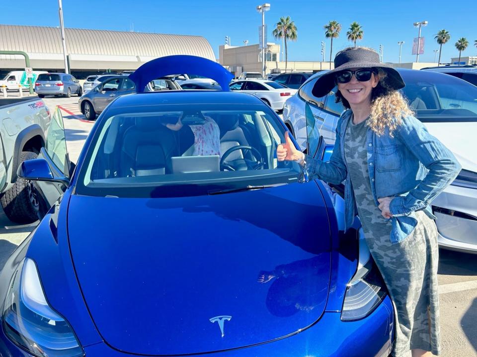 Woman stood with Tesla 3 in car park.