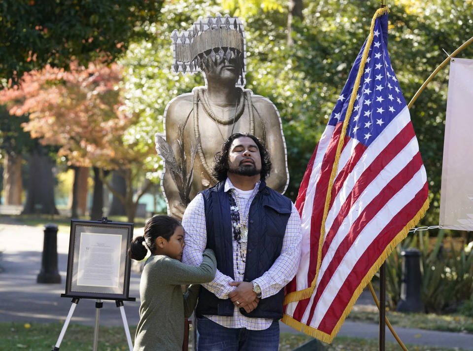 Jesse Tarango, right, chairman of Wilton Rancheria, is hugged by his son Jesse while standing in front of a enlarged photo of a statue of the late William Franklin Sr. during a groundbreaking ceremony for a Native American monument at Capitol Park in Sacramento, Calif., Monday, Nov. 14, 2022. The actual statue of Franklin will replace a statue of Fr. Junipero Serra whose statue was torn down by protesters in 2020. The new statue is expected to be placed in the park in early 2023. (AP Photo/Photo/Rich Pedroncelli)