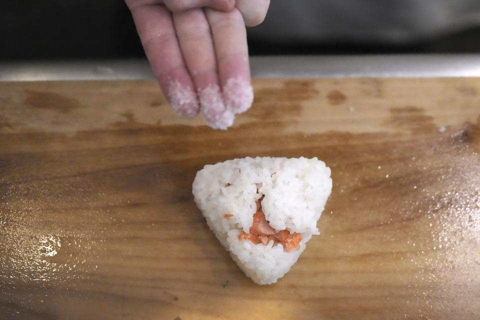 Yosuke Miura makes a rice ball with pieces of grilled salmon at Onigiri Asakusa Yadoroku, Tokyo's oldest onigiri restaurant, on June 3, 2024, in Tokyo. The word "onigiri" just became part of the Oxford English Dictionary this year. The humble sticky-rice ball, a mainstay of Japanese food, has entered the global lexicon. (AP Photo/Eugene Hoshiko)