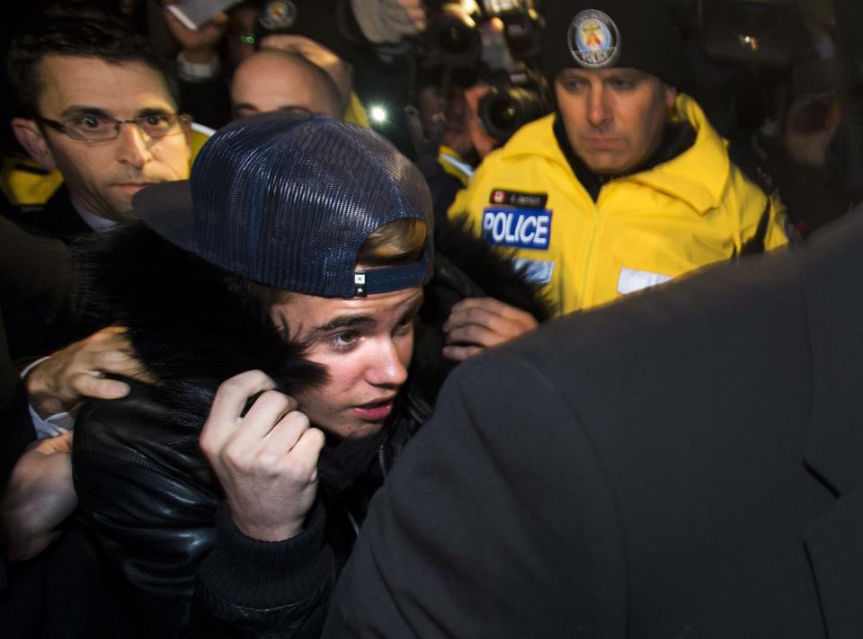 Canadian musician Justin Bieber is swarmed by media and police officers as he turns himself in to city police for an expected assault charge, in Toronto, on Wednesday, Jan. 29, 2014. A police official said the charge has to do with an alleged assault on a limo driver in December. (AP Photo/The Canadian Press, Nathan Denette)