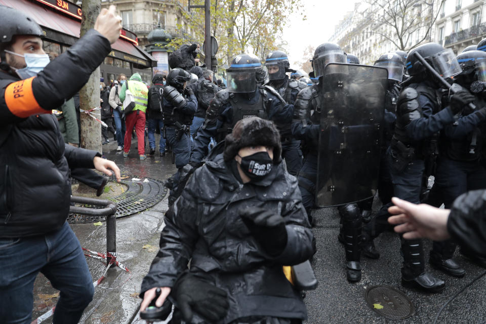 A member of the press, left, films riot police officers during a protest, Saturday, Dec.12, 2020 in Paris. Protests are planned in France against a proposed bill that could make it more difficult for witnesses to film police officers. (AP Photo/Lewis Joly)