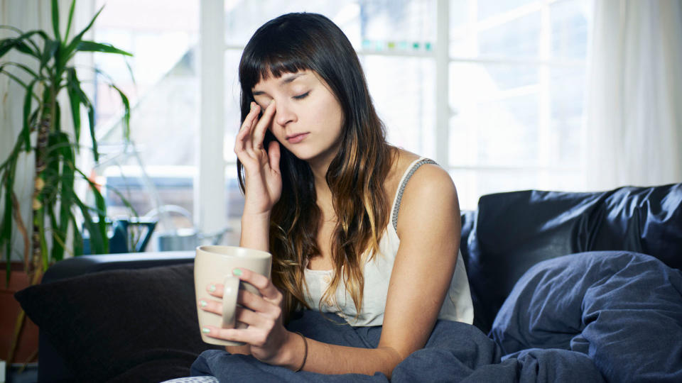 Tired woman wiping her eyes sat on the edge of a bed