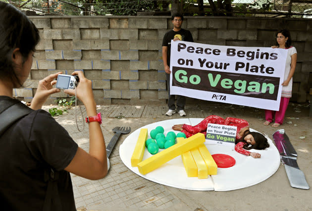 An onlooker takes a photograph of a People for the Ethical Treatment of Animals (PeTA) activist attired to look like a pice of meat within a meal as she lies on a huge plate during a demonstration in Bangalore on September 21, 2012. The activists staged the demonstration to urge public to go vegan and stop violence against animals to mark the International Day of Peace. AFP PHOTO/Manjunath KIRAN