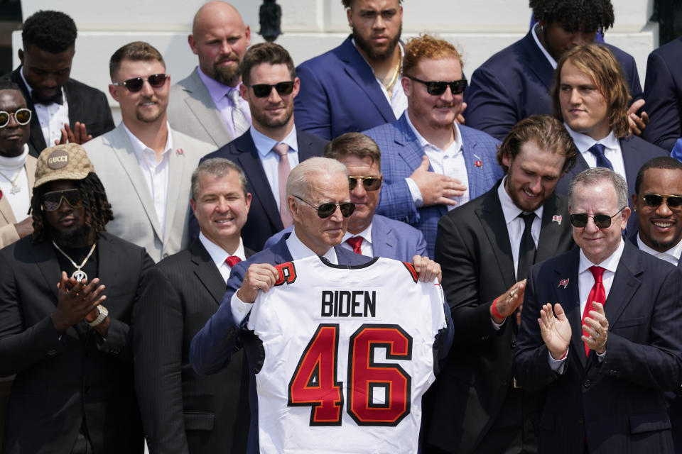 President Joe Biden, surrounded by members of the Tampa Bay Buccaneers, poses for a photo holding a jersey during a ceremony on the South Lawn of the White House, in Washington, Tuesday, July 20, 2021, where Biden honored the Super Bowl Champion Tampa Bay Buccaneers for their Super Bowl LV victory. (AP Photo/Andrew Harnik)