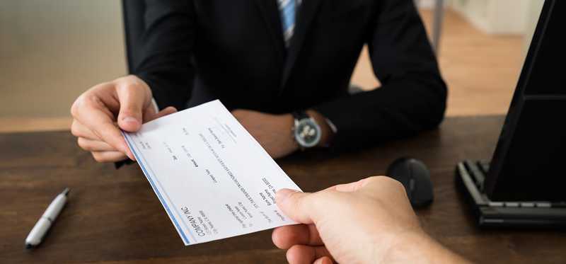 Person in suit handing over a check to another person.