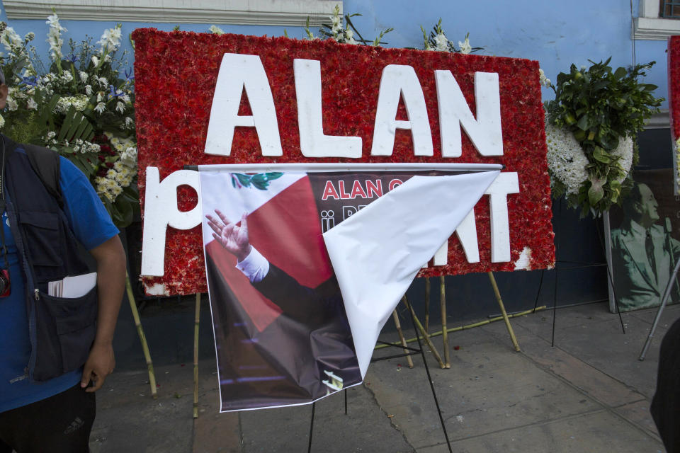 A banner of Peru's late President Alan Garcia flips up amid funeral flowers inside the political party headquarters where his wake takes place in Lima, Peru, Friday, April 19, 2019. Garcia shot himself in the head and died Wednesday as officers waited to arrest him in a massive graft probe that has put the country's most prominent politicians behind bars and provoked a reckoning over corruption. (AP Photo/Rodrigo Abd)