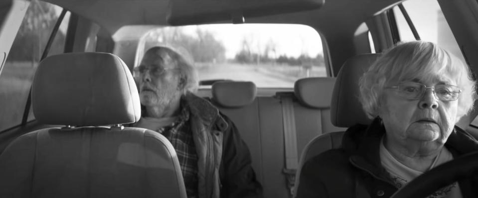 june squibb as kate in nebraska, a woman with oval glasses driving a car. bruce dern, as woody, is sitting in the back seat of the car. the image is in black and white, and kate and woody aren't looking towards each other