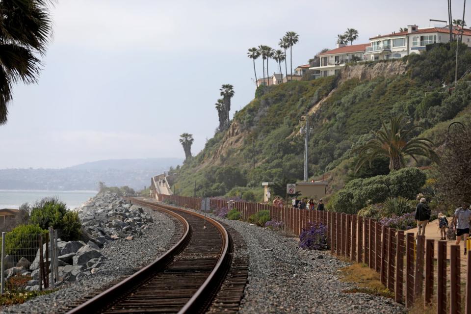 A railroad track curves seaward below blufftop homes.