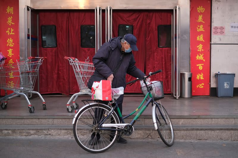 A man wearing a face mask stands next to his bicycle outside of a supermarket, as the country is hit by an outbreak of the new coronavirus, in Beijing