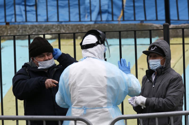 A Hospital worker distributes PPE to people waiting in line to be tested for coronavirus (COVID-19) outside Elmhurst Hospital Center in New York