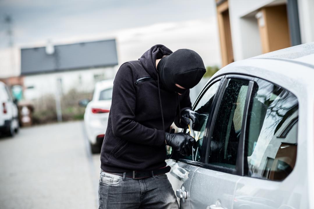 Car thief trying to break into a car with a screwdriver. Car thief, car theft.