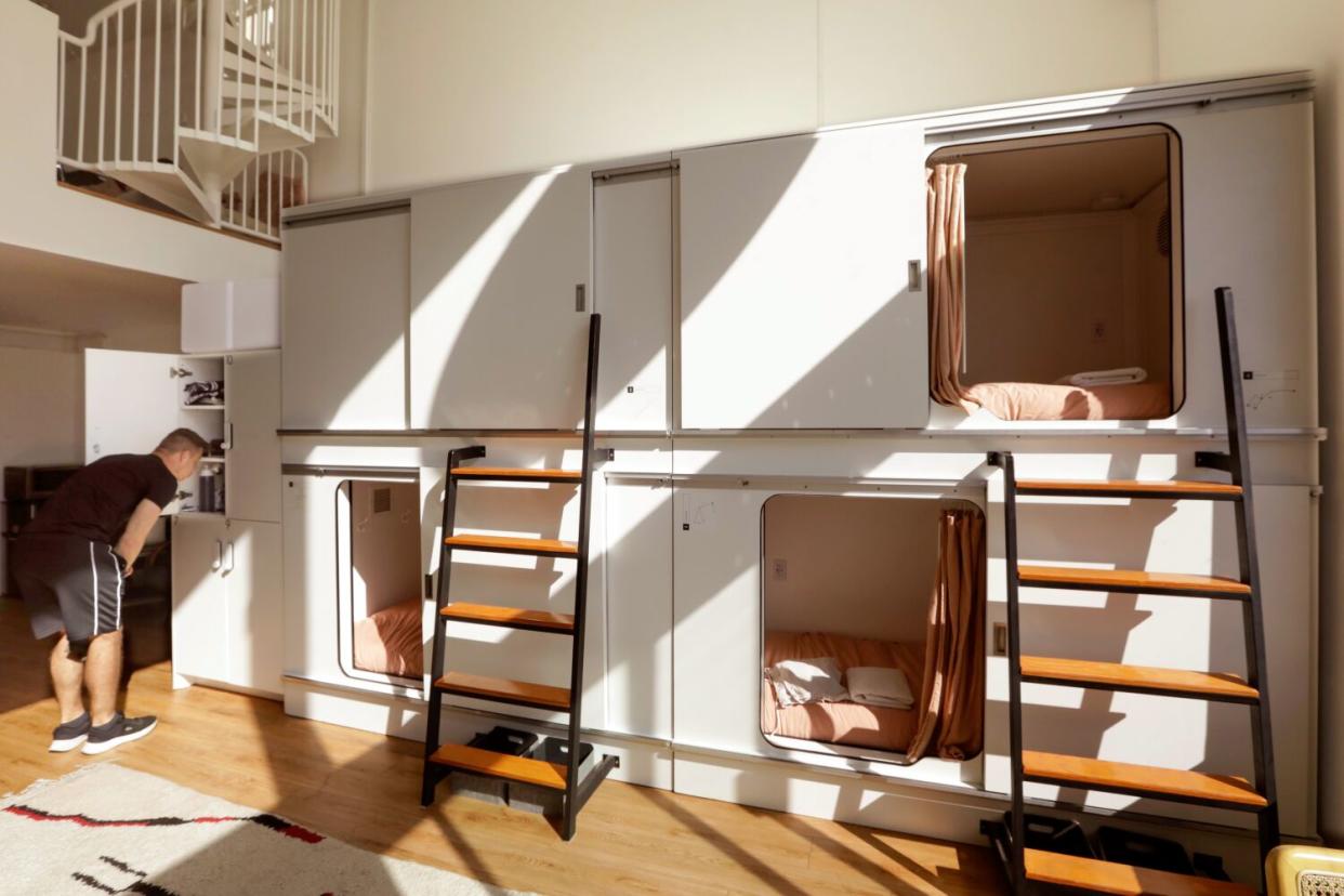 A man bending down to look through one of many doorways visible in a multilevel sleeping pod.