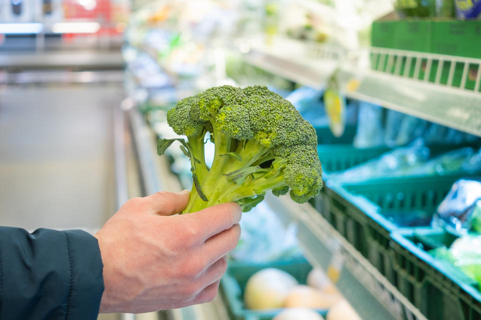 A man's hand takes broccoli from a drawer in a supermarket. The concept of choosing and buying products in a store, sales.