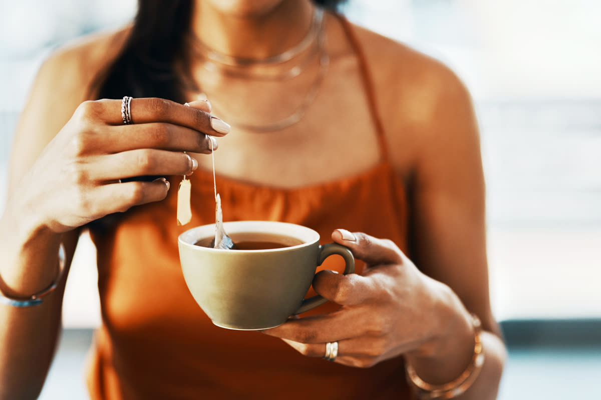 A woman dips a bag of tea in and out of the hot, steaming water inside her cup. 