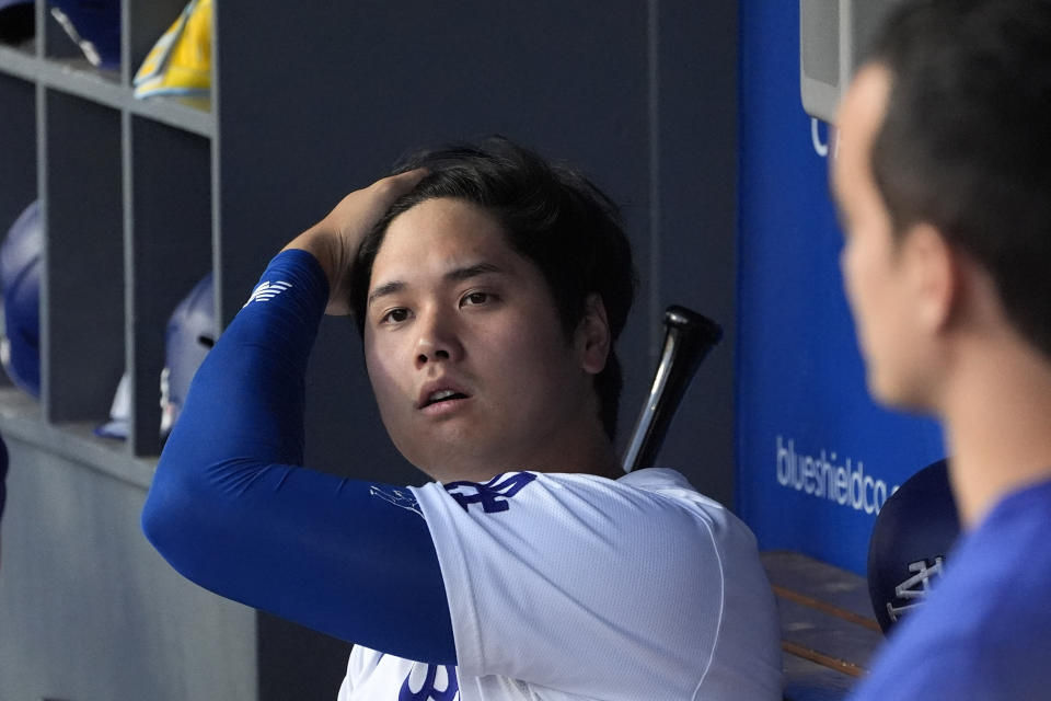 Los Angeles Dodgers' Shohei Ohtani, left, runs his fingers through his hair in the dugout as his interpreter Will Ireton stands by prior to a baseball game against the Milwaukee Brewers Friday, July 5, 2024, in Los Angeles. (AP Photo/Mark J. Terrill)