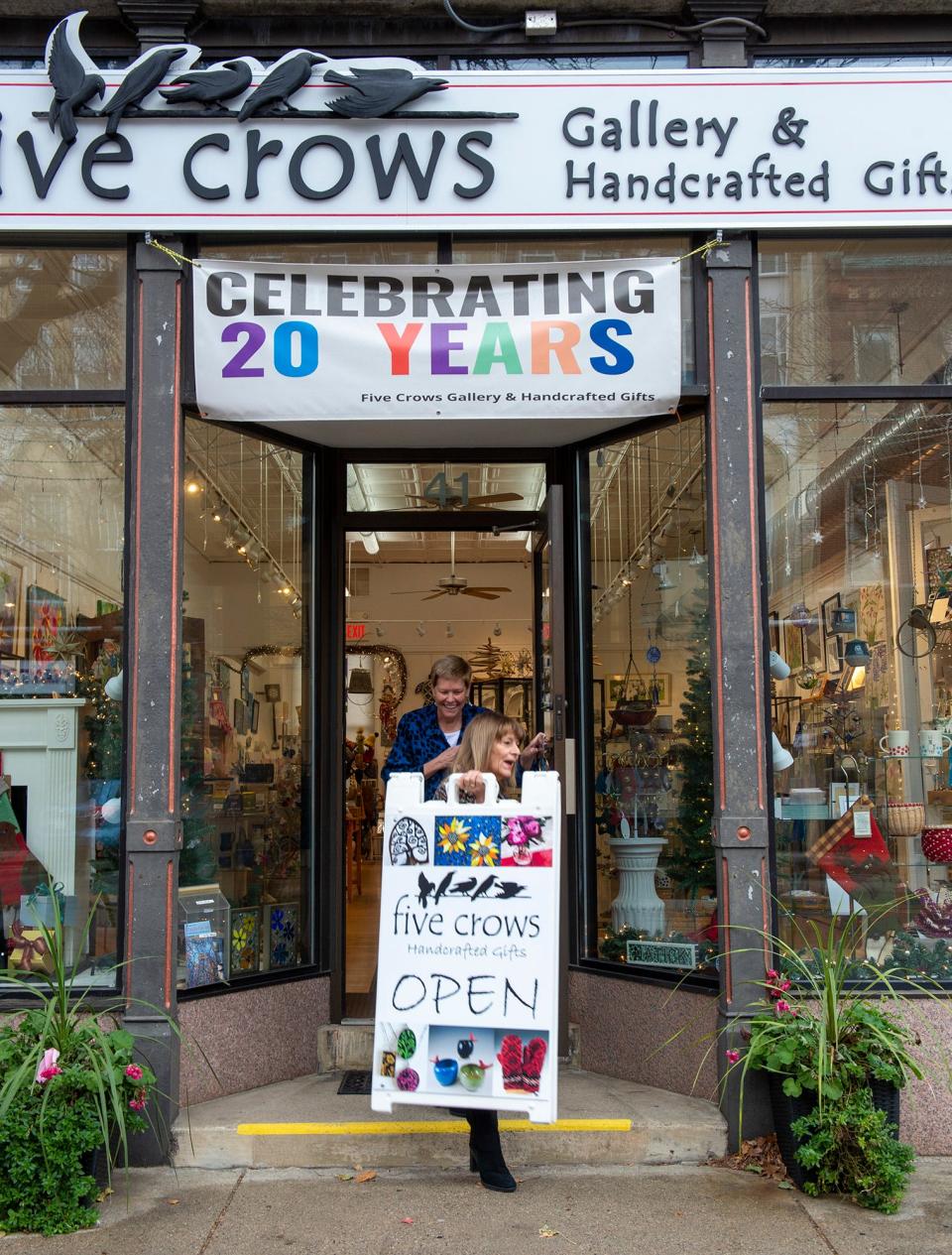 Sherry Anderson, one of three co-owners of Five Crows Gallery & Handcrafted Gifts in Natick, and Stephanie Childs, with sign, open the store on Nov. 25. Five Crows is celebrating its 20th anniversary with an open house from 5-8 p.m. on Dec. 8.