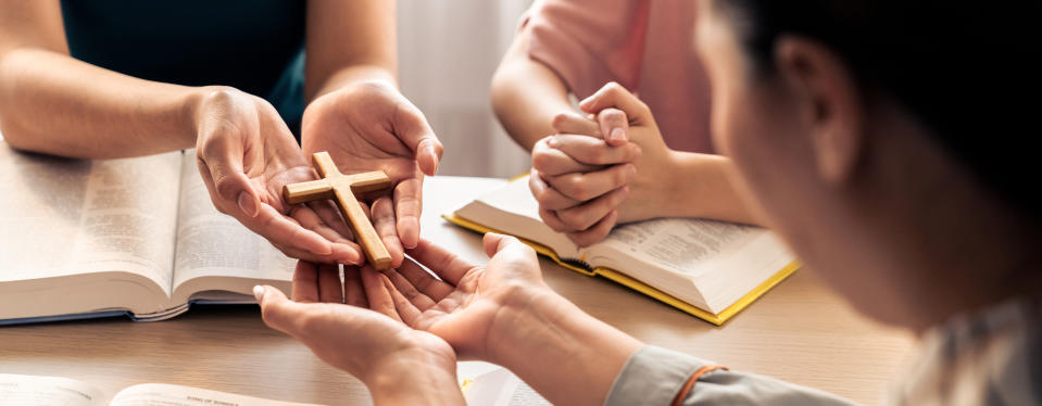 someone being handed a cross with bibles scattered around the table