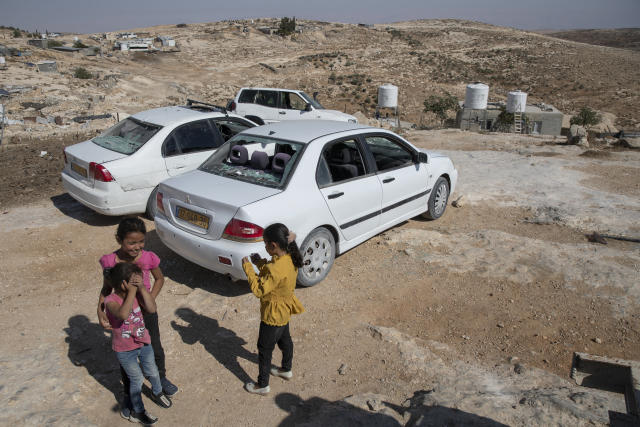Girls play around smashed vehicles following a settlers' attack from nearby settlement outposts on the Palestinian Bedouin community, in the West Bank village of al-Mufagara, near Hebron, Thursday, Sept. 30, 2021. An Israeli settler attack last week damaged much of the village’s fragile infrastructure. (AP Photo/Nasser Nasser)