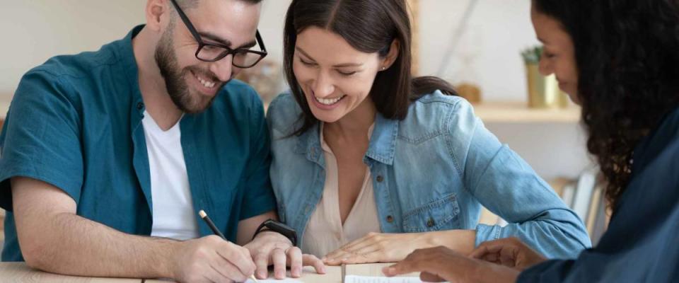 Happy young married couple signing contract, making successful deal, smiling young husband wearing glasses putting signature on legal documents, purchasing new house, taking loan or mortgage