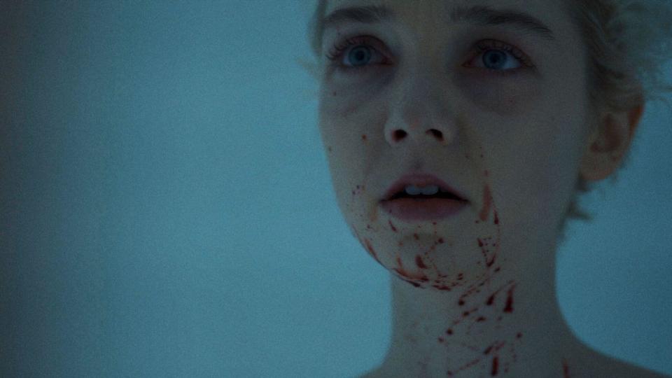 A young woman splattered with blood stares into a mirror in "Come True"