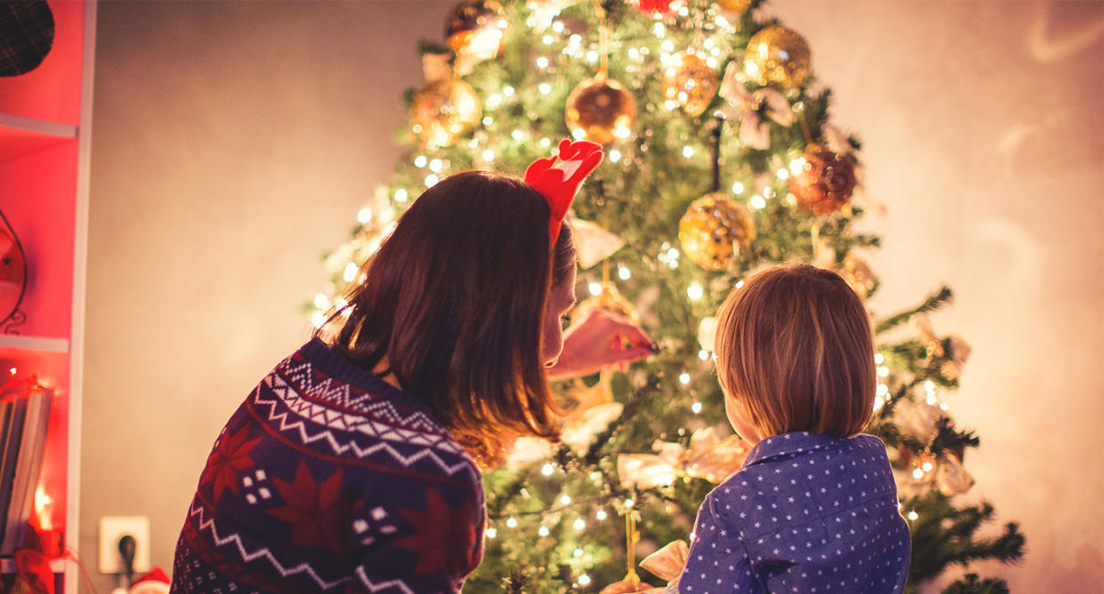 Mother and son hanging Christmas tree lights, pictured in front of the decorated tree. (Getty Images)