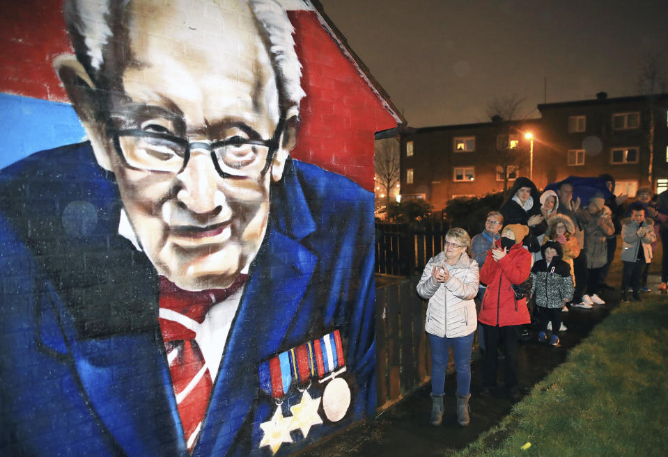 Local residents join a national clap beside a mural of Captain Sir Tom Moore in East Belfast, Northern Ireland, Wednesday, Feb. 3, 2021. Captain Moore passed away Tuesday after being treated with Covid-19 and was known for his achievements raising millions of pounds for the NHS charity during the Covid-19 pandemic. (AP Photo/Peter Morrison)