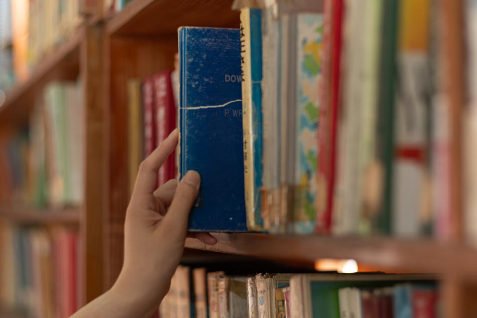 someone picking up a book from a library shelf