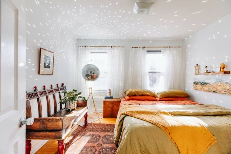 Light reflects off disco ball in white bedroom with rust accents.