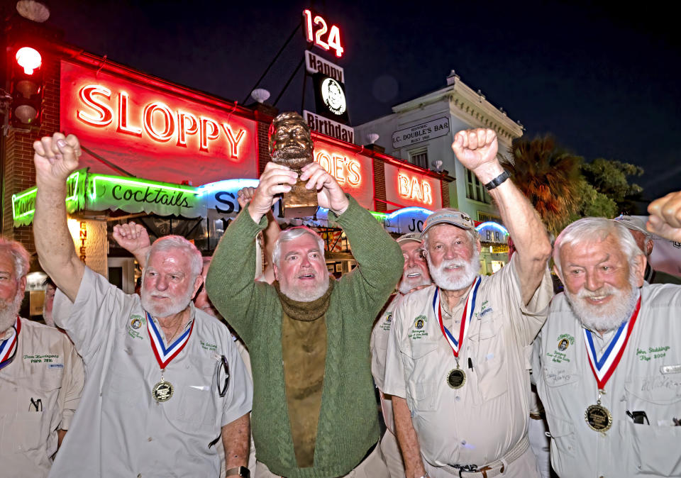 In this Saturday, July 22, 2023, photo provided by the Florida Keys News Bureau, Gerrit Marshall, center, hoists his trophy after winning the Hemingway Look-Alike Contest at Sloppy Joe's Bar in Key West, Fla. After 11 years of competing Marshall, a Madison, Wisc., resident, finally achieved success on his 68th birthday. Flanking Marshall, from left, are previous winners including Tom Grizzard, Wally Collins and John Stubbings. The competition was a highlight of the annual Hemingway Days festival that ends Sunday, July 23. Ernest Hemingway lived in Key West throughout most of the 1930s. (Andy Newman/Florida Keys News Bureau via AP)