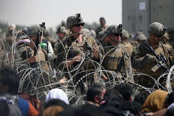 PHOTO: FILE - US soldiers stand guard behind barbed wire as Afghans sit on a roadside near the military part of the airport in Kabul, Aug. 20, 2021, hoping to flee from the country after the Taliban's military takeover of Afghanistan. (Wakil Kohsar/AFP via Getty Images, FILE)
