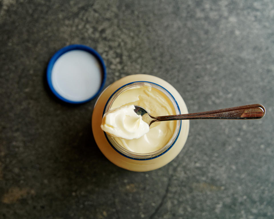 Jar of yogurt with spoon, on a dark surface, next to open lid