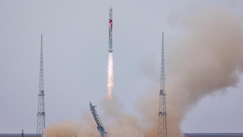 rocket lifting off between two launch towers and sending out a  cloud of dust behind