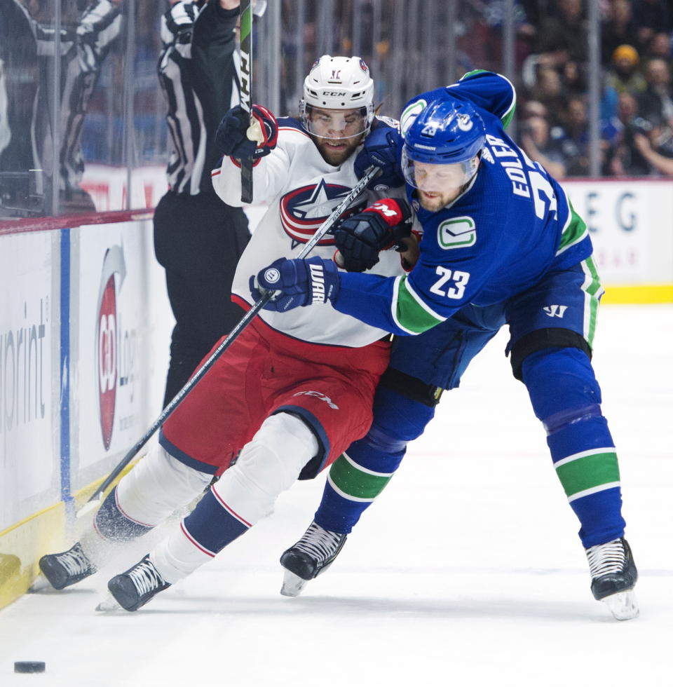 Vancouver Canucks defenseman Alexander Edler (23) fights for control of the puck with Columbus Blue Jackets centre Kevin Stenlund (11) during the first period of an NHL hockey game, in Vancouver, British Columbia, Sunday, March 8, 2020. (Jonathan Hayward/The Canadian Press via AP)
