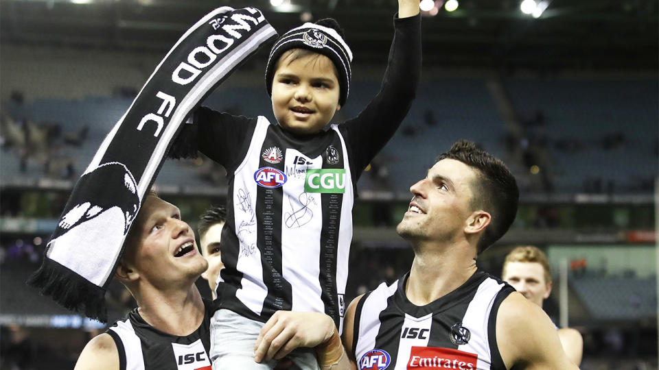 Collingwood mascot, Kyron McGuire, is chaired off the ground by Adam Treloar of the Magpies and Scott Pendlebury of the Magpies during the 2019 AFL round 07 match between the Collingwood Magpies and the Port Adelaide Power at Marvel Stadium on May 03, 2019 in Melbourne, Australia. (Photo by Dylan Burns/AFL Photos)