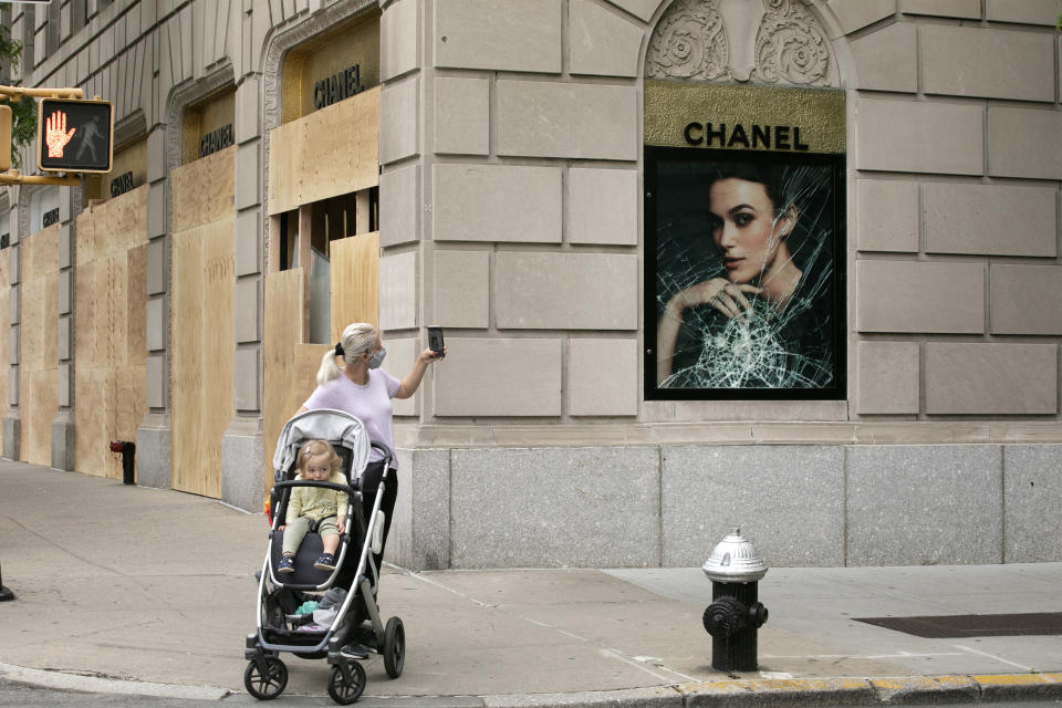 A woman photographs a smashed Chanel store window, Tuesday, June 2, 2020, on Madison Avenue in New York. Protesters broke the window in reaction to the death of George Floyd, a black man who died after being restrained by Minneapolis police officers on May 25. The New York City immortalized in song and scene has been swapped out for the last few months with the virus version. In all the unknowing of what the future holds, there’s faith in that other quintessential facet of New York City: that the city will adapt. (AP Photo/Mark Lennihan)