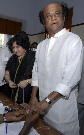 FILE PHOTO: Tamil superstar Rajinikanth (R) gets his finger marked with ink before casting his ballot as his wife Lata watches at a polling station in Chennai May 13, 2009. REUTERS/Babu/File Photo